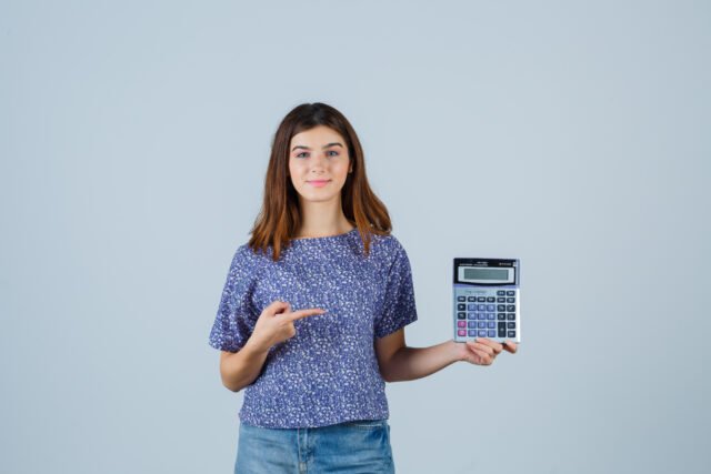 young girl in blouse, jeans pointing at calculator and looking confident , front view.